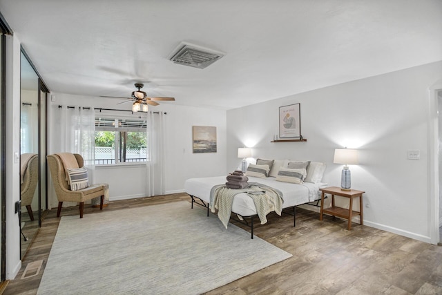 bedroom with a ceiling fan, wood finished floors, visible vents, and baseboards