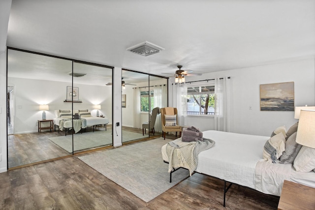 bedroom with two closets, wood finished floors, visible vents, and baseboards