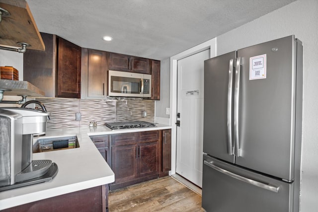 kitchen with stainless steel appliances, light countertops, backsplash, light wood-style floors, and dark brown cabinetry