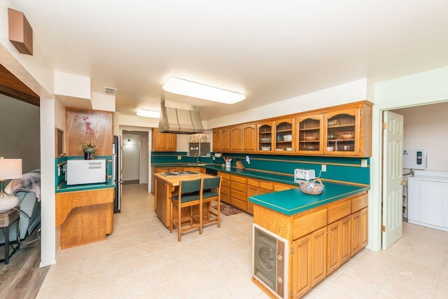 kitchen with brown cabinets, visible vents, glass insert cabinets, a sink, and ventilation hood