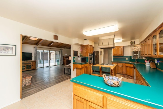 kitchen with light tile patterned floors, dark countertops, appliances with stainless steel finishes, brown cabinetry, and glass insert cabinets