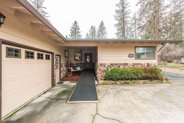 view of exterior entry featuring a garage, stone siding, and driveway