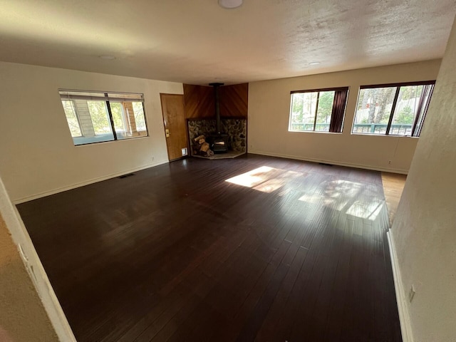 unfurnished living room with a wood stove, visible vents, plenty of natural light, and wood finished floors