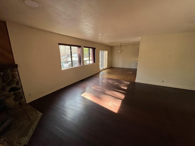 unfurnished living room with a textured ceiling, baseboards, and dark wood-type flooring