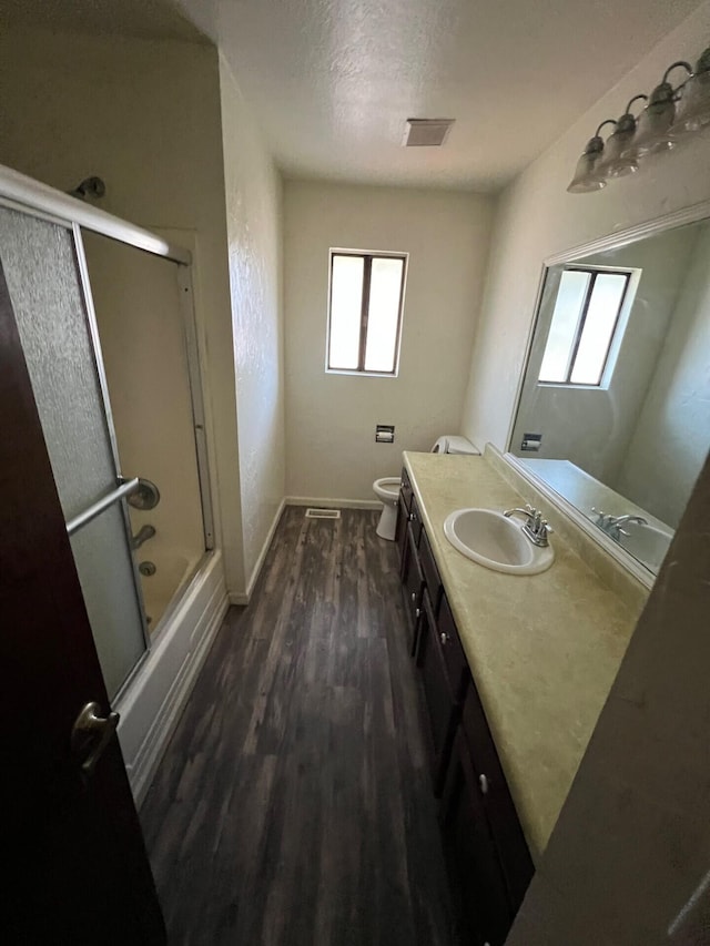 bathroom featuring toilet, enclosed tub / shower combo, vanity, wood finished floors, and baseboards