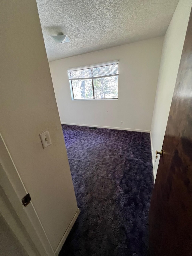 carpeted empty room featuring a textured ceiling and baseboards