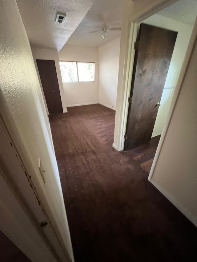 corridor featuring visible vents, dark carpet, and a textured ceiling