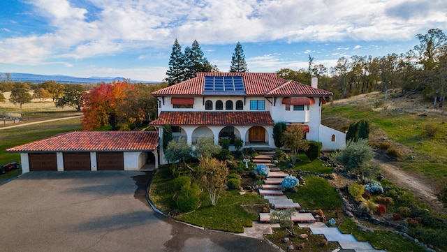 mediterranean / spanish-style home featuring a chimney, stairway, roof mounted solar panels, driveway, and a tiled roof