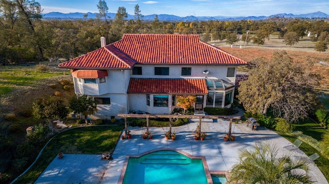 back of house featuring a mountain view, a tile roof, an outdoor pool, a chimney, and a patio area