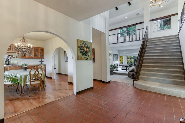 dining room with arched walkways, a towering ceiling, baseboards, stairs, and an inviting chandelier