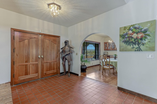 entryway with baseboards, arched walkways, tile patterned floors, a textured ceiling, and a chandelier