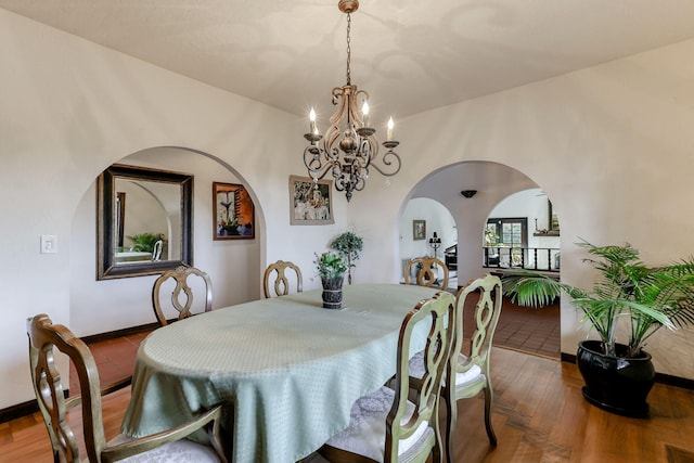 dining room with arched walkways, baseboards, an inviting chandelier, and wood finished floors