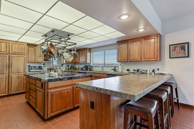 kitchen featuring a peninsula, a sink, a kitchen breakfast bar, backsplash, and brown cabinetry