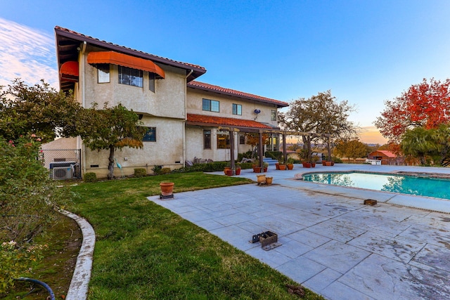 back of house with a yard, a patio, stucco siding, an outdoor pool, and a tiled roof