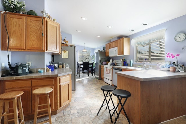 kitchen featuring white appliances, a kitchen breakfast bar, a peninsula, stone finish flooring, and a sink