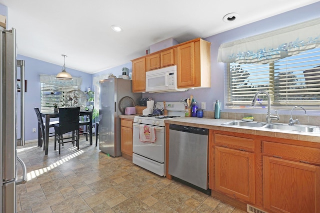 kitchen with pendant lighting, stainless steel appliances, light countertops, stone finish floor, and a sink