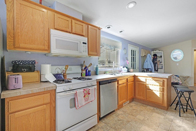 kitchen featuring recessed lighting, stone finish floor, a sink, white appliances, and a peninsula