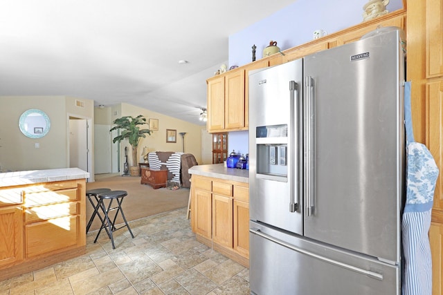 kitchen featuring lofted ceiling, stone finish flooring, tile countertops, and stainless steel refrigerator with ice dispenser