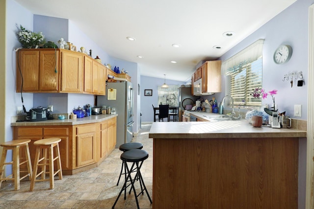 kitchen featuring stone finish floor, freestanding refrigerator, a peninsula, light countertops, and a sink