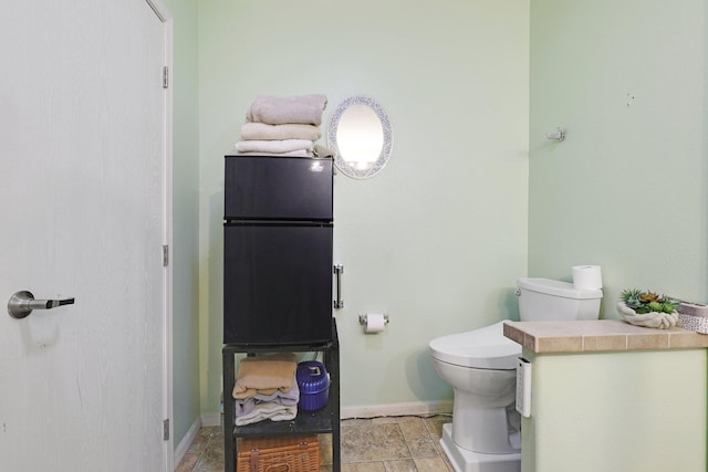 bathroom featuring toilet, stone finish floor, and baseboards