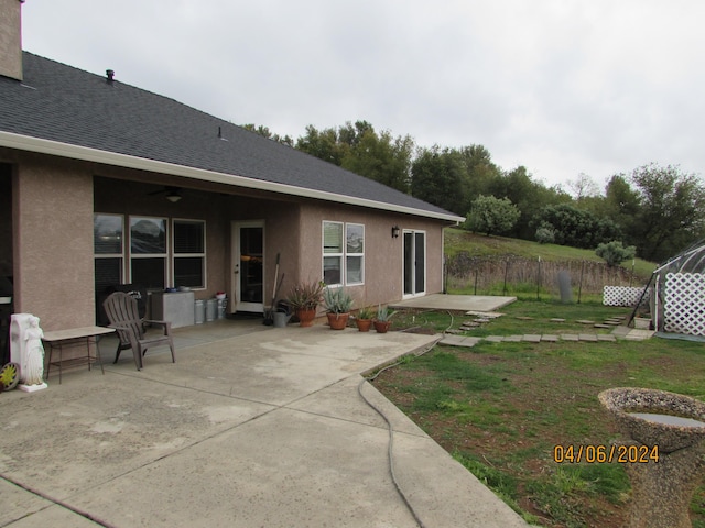 exterior space featuring a shingled roof, a lawn, fence, a patio area, and stucco siding