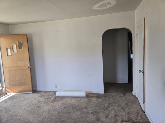 spare room featuring baseboards, dark carpet, and arched walkways