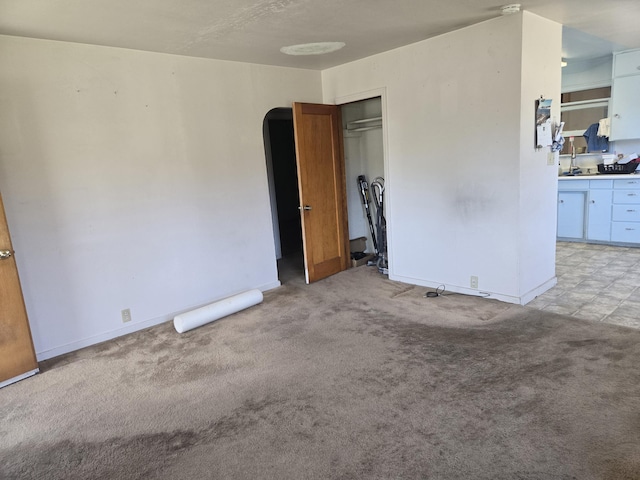 spare room with arched walkways, light colored carpet, a sink, and baseboards