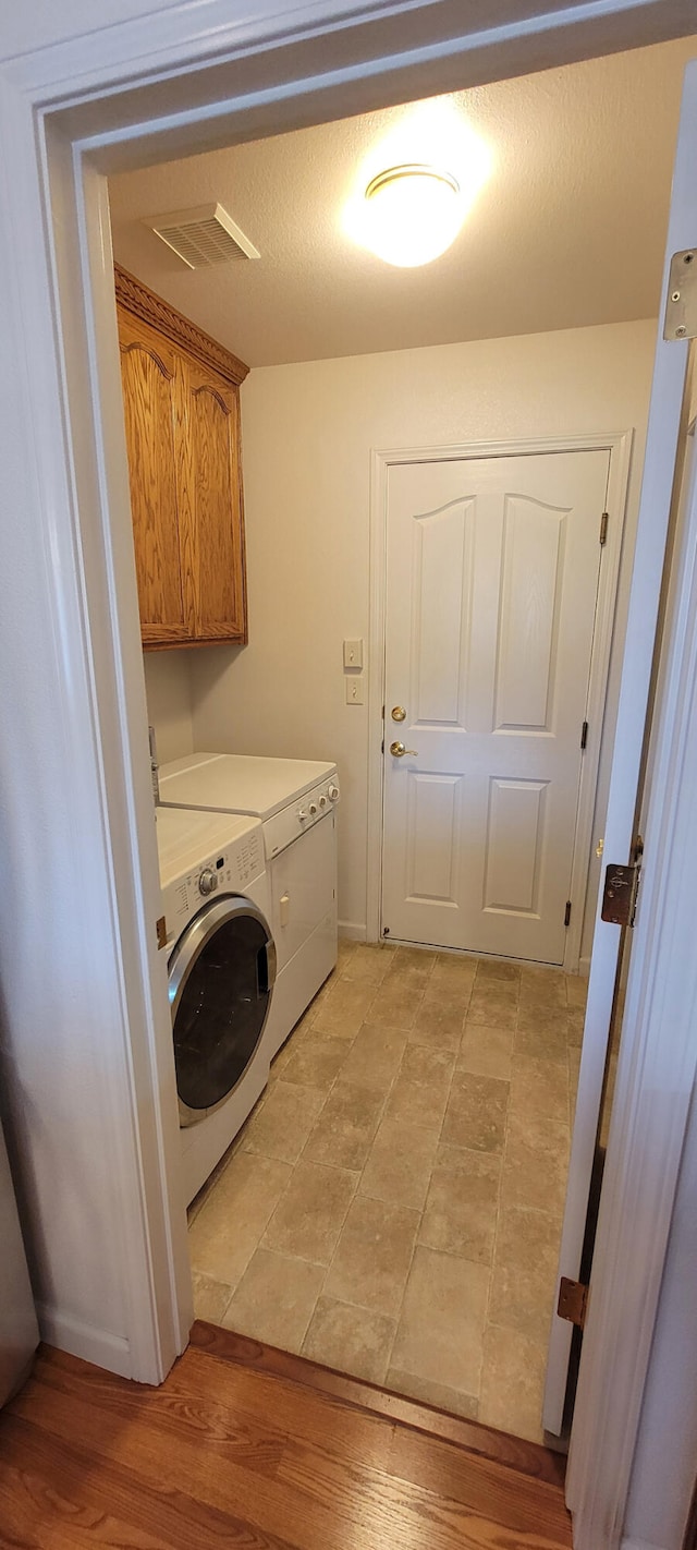 laundry area featuring cabinet space, visible vents, light wood-style flooring, a textured ceiling, and washing machine and dryer