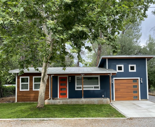 contemporary house with a front yard, covered porch, driveway, and metal roof