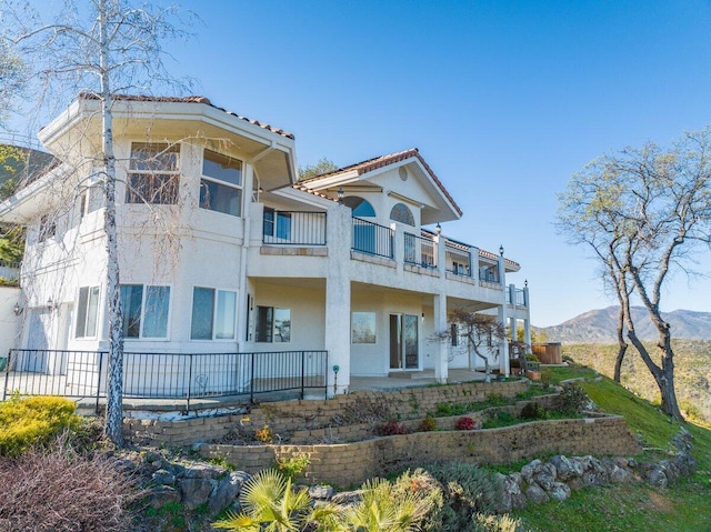 back of property with a balcony, a tile roof, a mountain view, and stucco siding