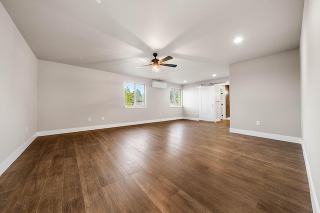 empty room with a barn door, a wall unit AC, dark wood finished floors, and baseboards