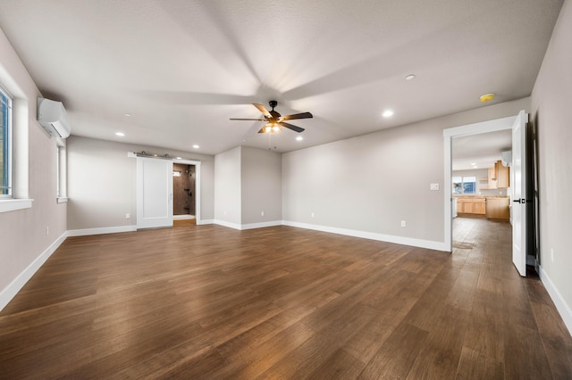 empty room with dark wood-style floors, recessed lighting, a wall mounted AC, a barn door, and baseboards