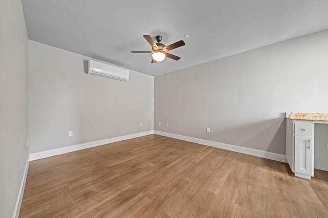 spare room with light wood-style floors, ceiling fan, baseboards, and a wall mounted AC