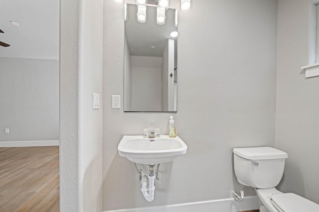 half bath with toilet, baseboards, and wood finished floors