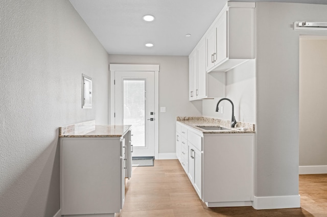 kitchen with baseboards, white cabinets, light stone counters, light wood-style floors, and a sink