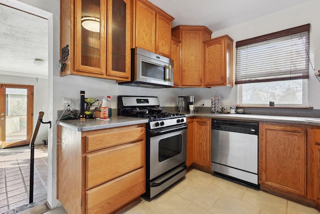 kitchen with brown cabinetry, glass insert cabinets, a wealth of natural light, and stainless steel appliances