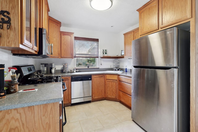 kitchen with a sink, light countertops, glass insert cabinets, appliances with stainless steel finishes, and brown cabinets