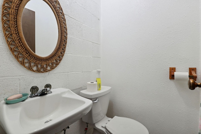 bathroom with concrete block wall, toilet, and a sink