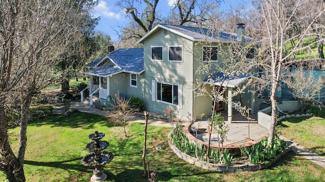 back of house featuring a shingled roof, a patio, a yard, and a chimney