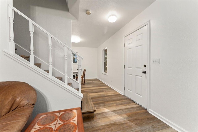 foyer entrance featuring a textured ceiling, stairway, baseboards, and wood finished floors