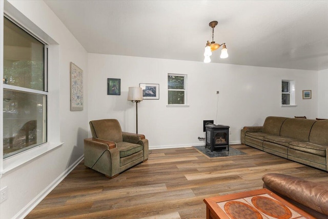 living room featuring a notable chandelier, wood finished floors, a wood stove, and baseboards