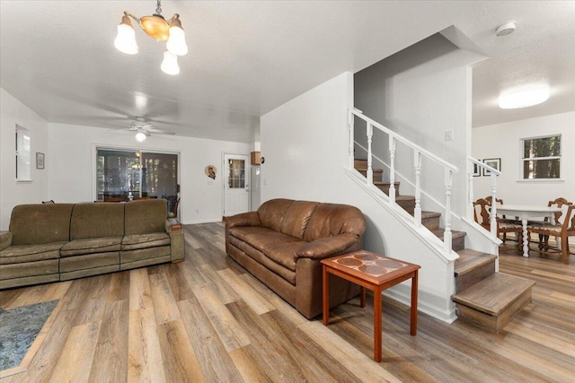 living area with ceiling fan with notable chandelier, wood finished floors, a textured ceiling, and stairs