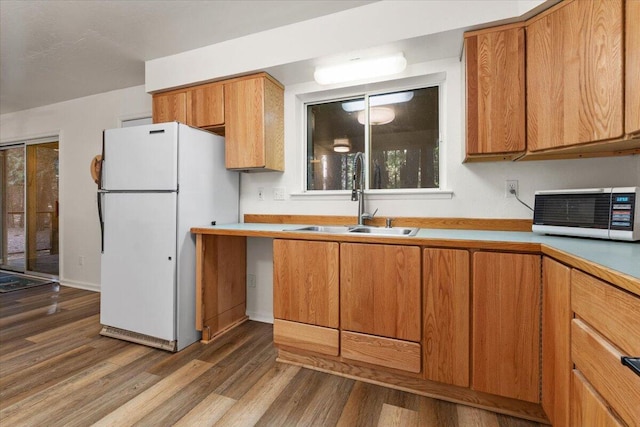 kitchen featuring wood finished floors, a sink, light countertops, freestanding refrigerator, and brown cabinetry