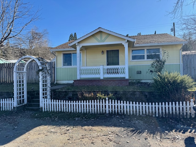 bungalow with a porch, fence, and a shingled roof