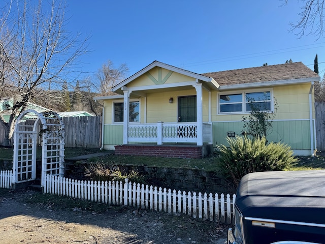 bungalow with covered porch, roof with shingles, and fence