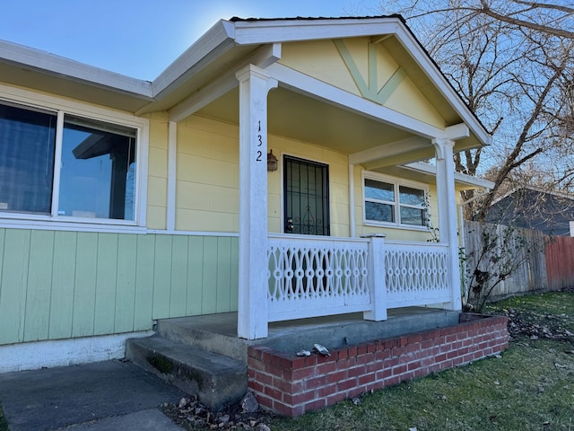 view of exterior entry with covered porch and fence