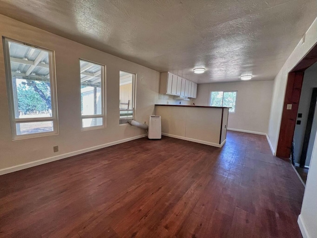 kitchen featuring dark wood finished floors, white cabinets, a textured ceiling, a peninsula, and baseboards