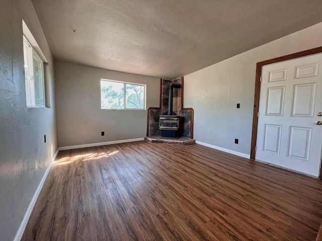 unfurnished living room with a textured ceiling, dark wood-style flooring, a wood stove, and baseboards