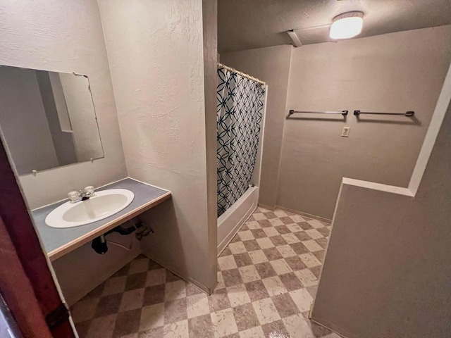 bathroom with a textured wall, curtained shower, a sink, and tile patterned floors