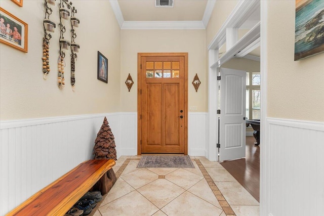 foyer with a wainscoted wall, ornamental molding, light tile patterned flooring, and visible vents